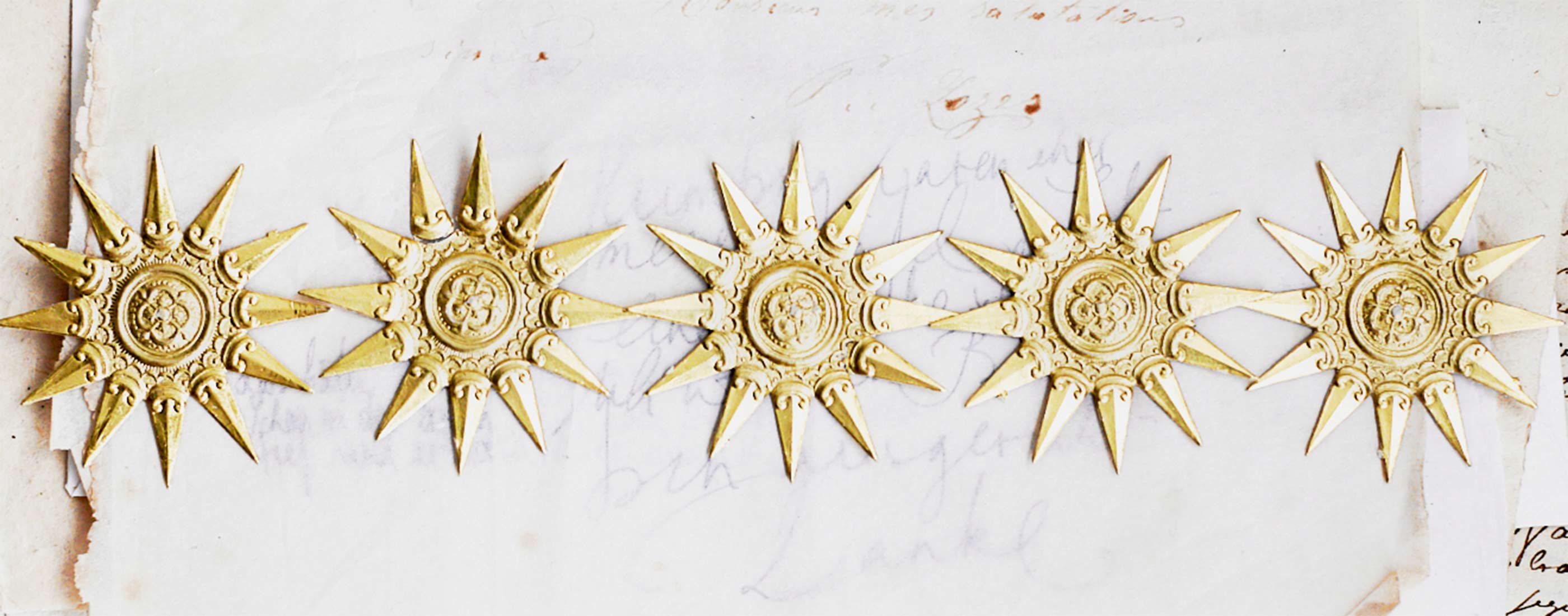 Reihe goldener Zierelemente in Sonnenform auf altem Papierhintergrund – symbolisch für wertvolle Bestseller-Produkte