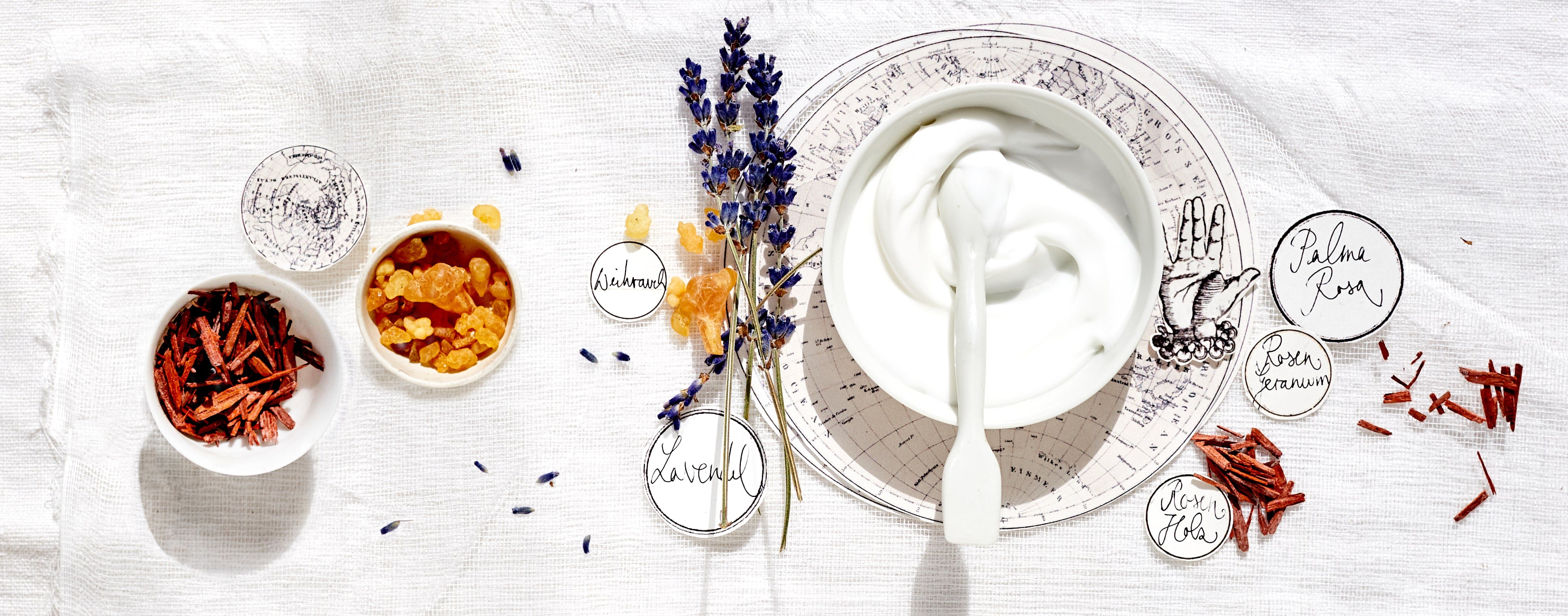 Natürliche Pflegezutaten wie Lavendel, Weihrauch, Sandelholz und eine weiße Creme in Schale auf Leinentuch – Symbol für sanfte Hautpflege