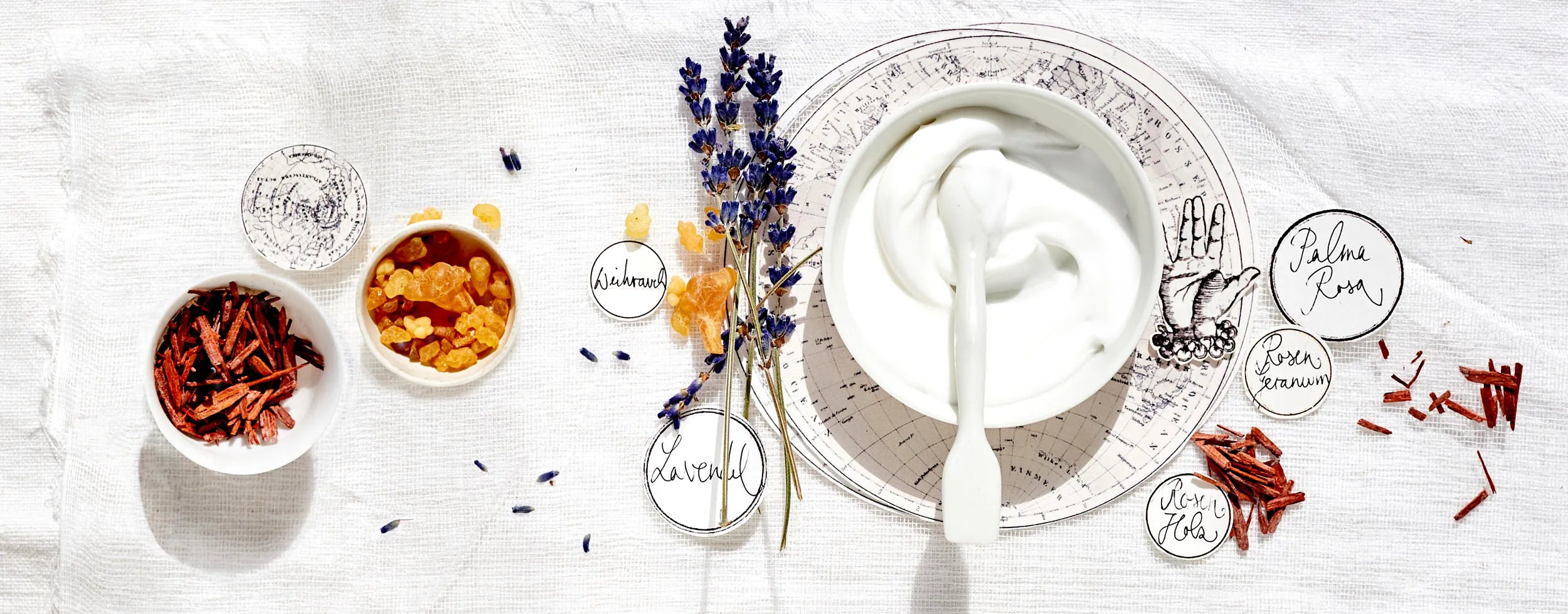 Natürliche Pflegezutaten wie Lavendel, Weihrauch, Sandelholz und eine weiße Creme in Schale auf Leinentuch – Symbol für sanfte Hautpflege