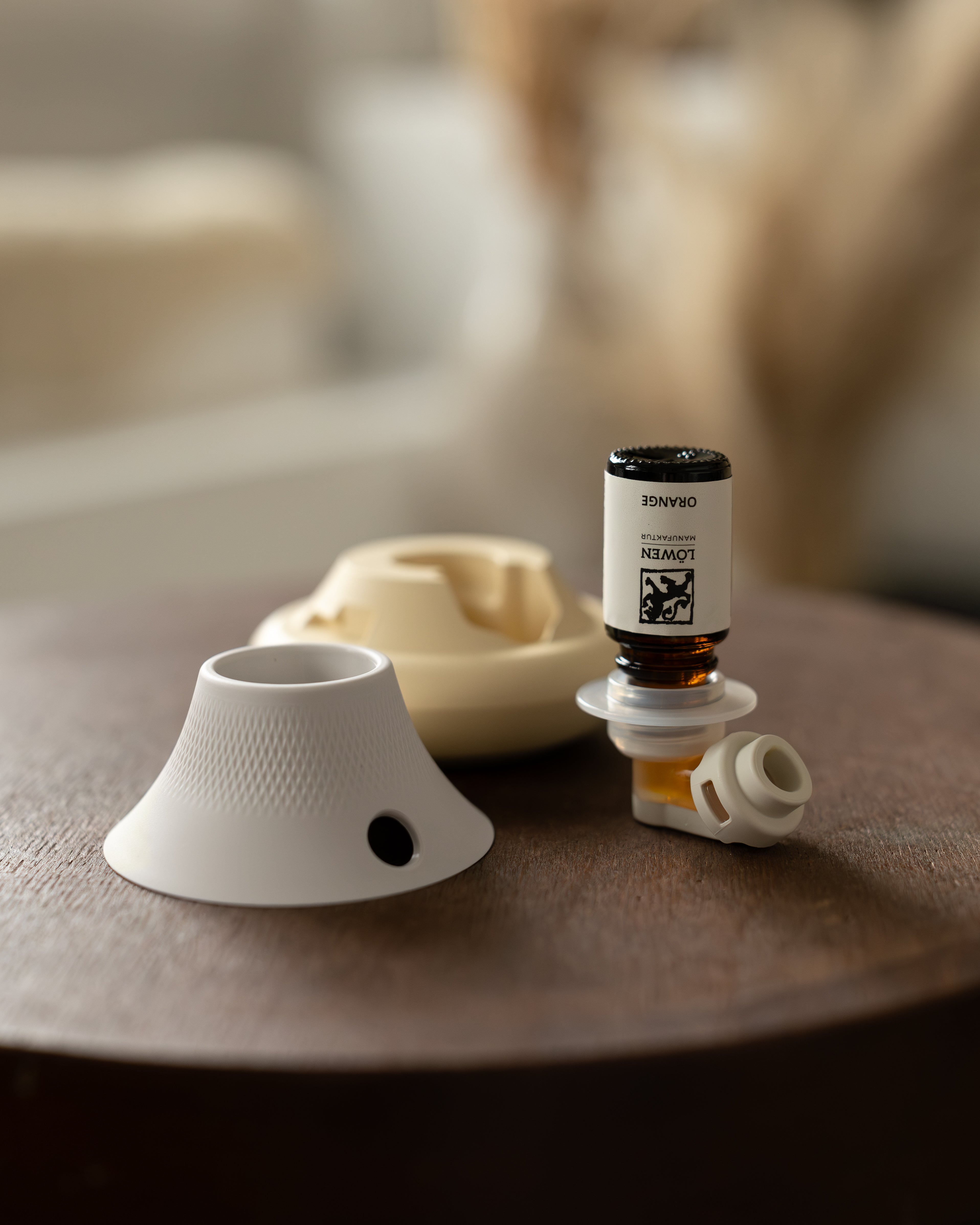 Ätherisches Orangenöl von der Löwen-Manufaktur in der Halterung eines modernen Duftgeräts, arrangiert mit weißem Aufsatz auf einem Holztisch – stilvolle Produktinszenierung für die Anwendung ätherischer Öle.