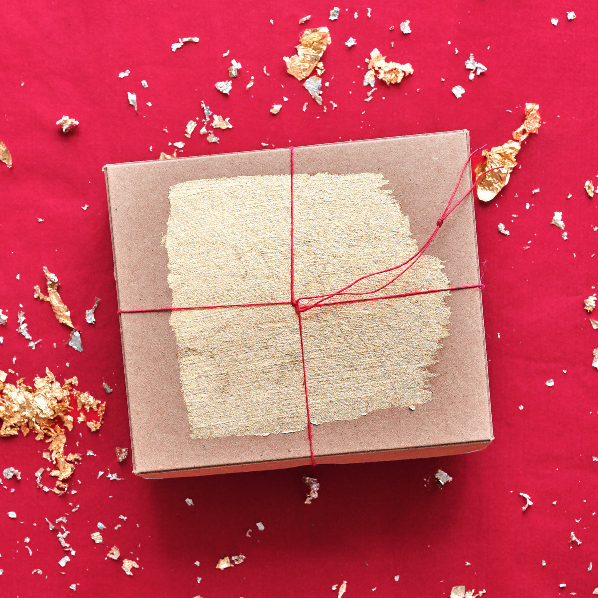 Geschlossene Geschenkbox mit rotem feinen Geschenkband und  Goldblattflocken verziert auf rotem Hintergrund.
