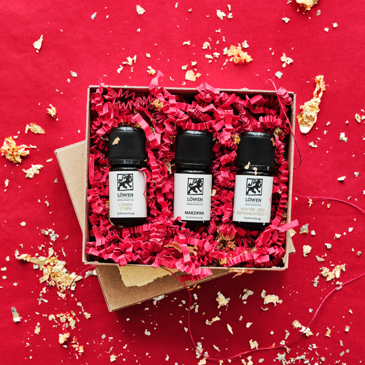 Geschenkbox mit drei Winterdüften in rotem Sizzel Papier mit Goldblattflocken verziert auf rotem Hintergrund.